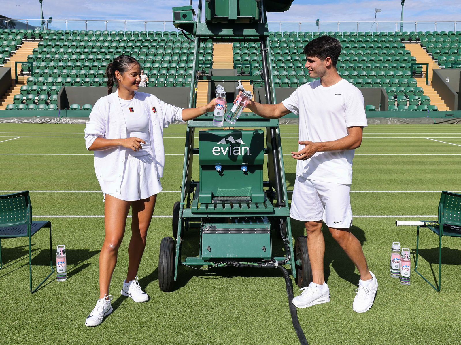 A photo of Emma Raducanu and Carlos Alcaraz clinking their water bottles together on a tennis court in London England on...